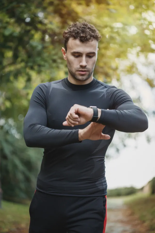 Man in a long-sleeve training top checking his watch outdoors