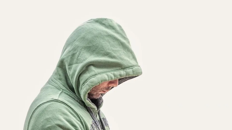 Man in a green hoodie with the hood up, looking down