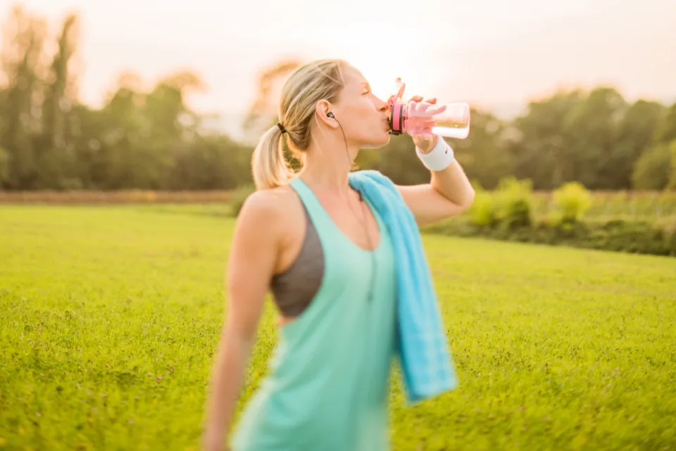 Woman in a tank top drinking water outdoors after a workout