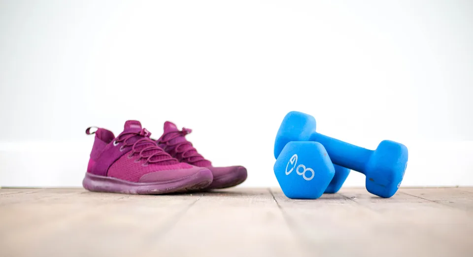 Purple training shoes next to blue dumbbells on a wooden floor